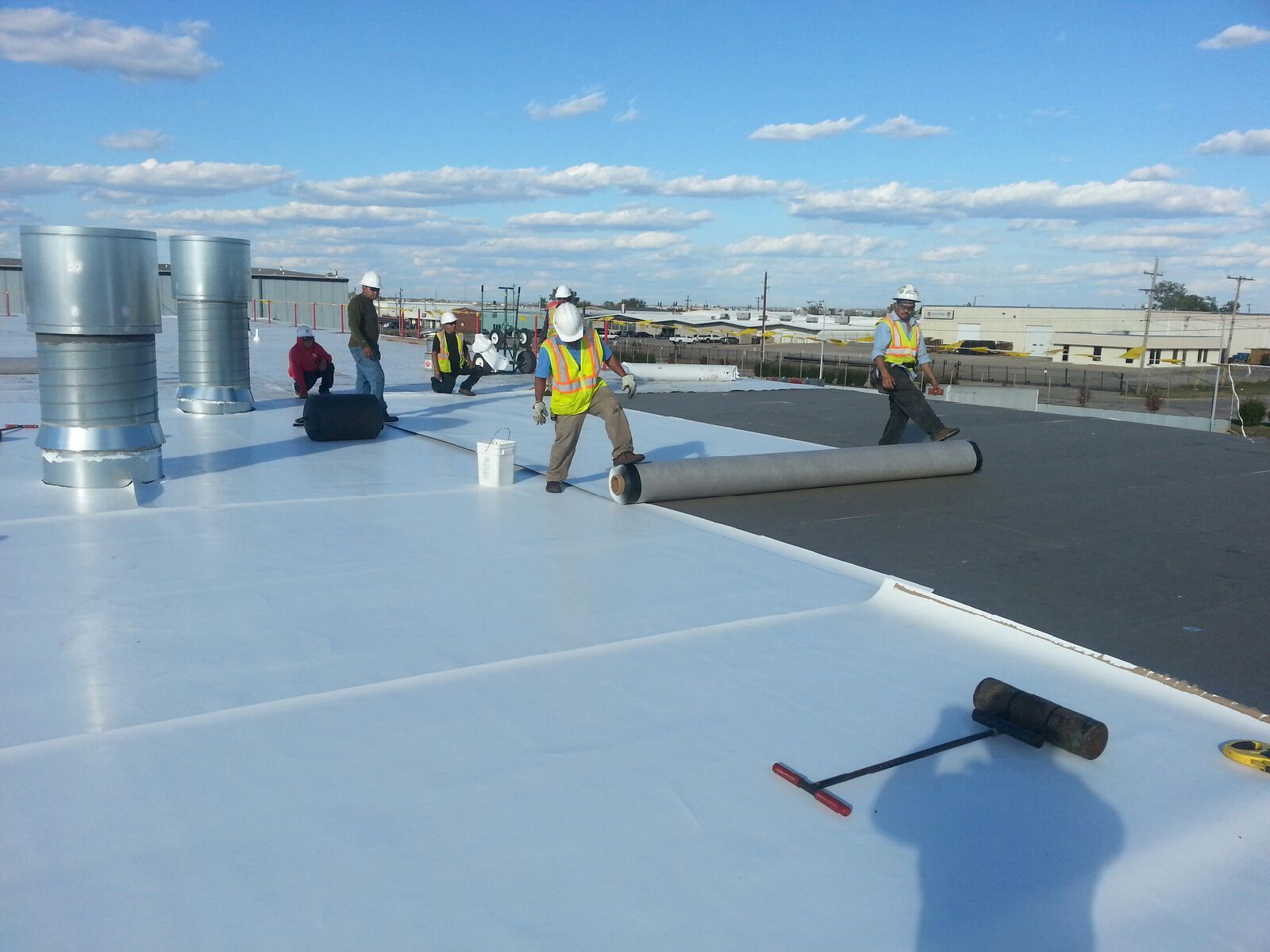 Construction workers installing white roofing membrane on commercial building roof