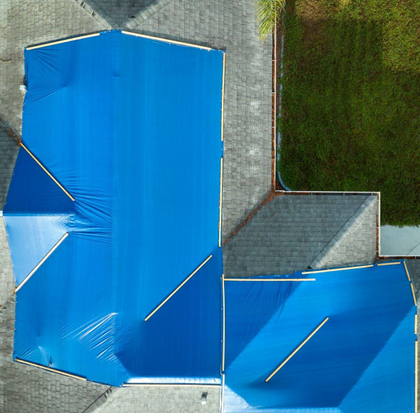 Aerial view of blue tarps covering sections of a house roof.